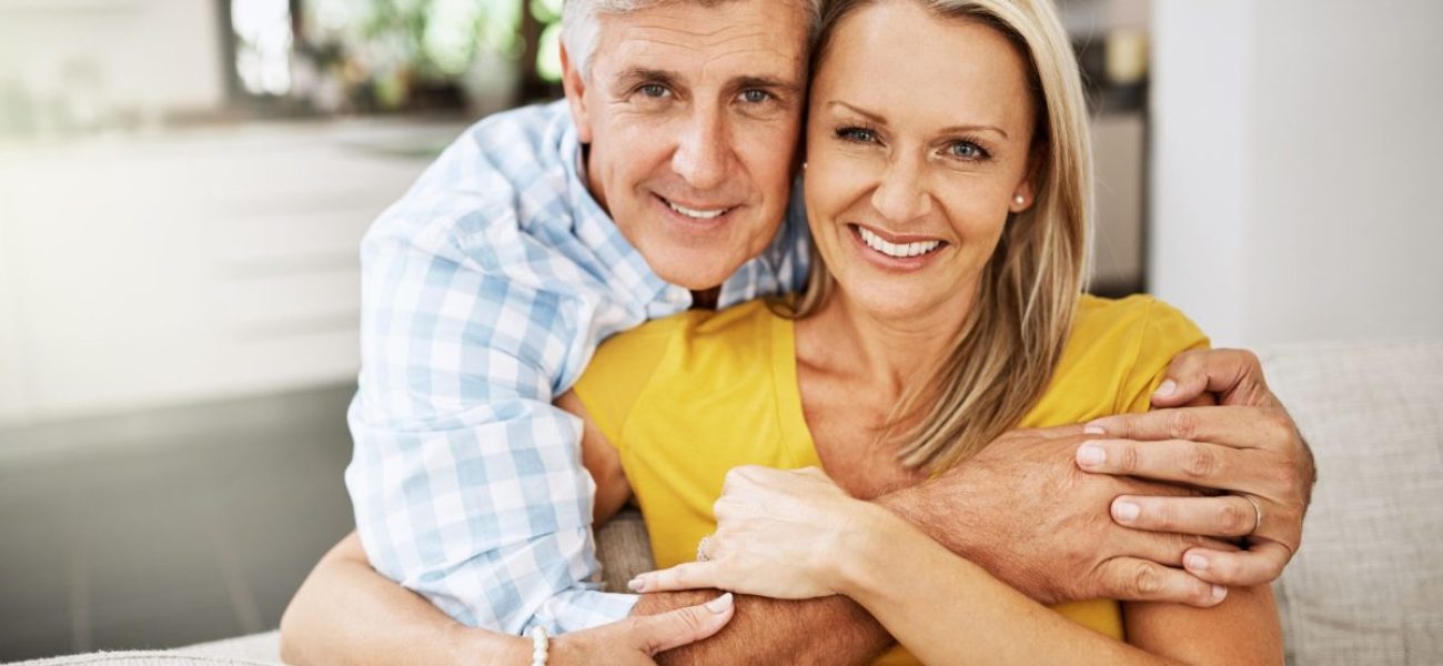 Happy, in love and affectionate senior couple hugging on the sofa in the living at room, enjoying time together and their retirement. Portrait of a happy man and woman bonding and smiling at home.